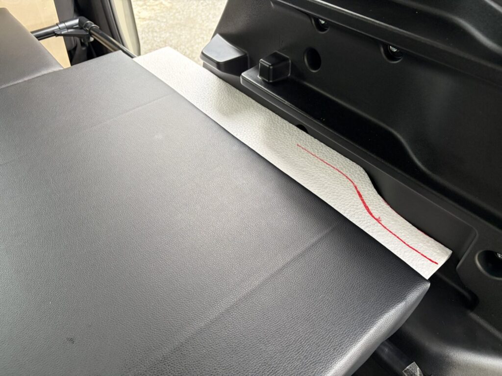 ベッドキット大詰め!複雑な「隙間」を埋めていく
前回の記事で、就寝のメインとなる大きな座面クッションが完成しました。今回は、さらに快適なフルフラット空間を目指して、ベッドと車の壁の間にできる「隙間」を埋めるパーツを作っていきます。
この隙間部分は、車のボディの内張りに合わせた複雑なカーブになるので、まっすぐ切るだけの今までとは違い、作っていくのが難しそうです…!
失敗しない!発泡スチロールを使った「型取り」の裏技
土台となる木材をいきなり切って失敗するのは怖いですよね。そこで考えたのが、加工しやすい発泡スチロールを使った型取りです。
まずは発泡スチロールを大まかに切り出し、車の内張りに合わせながら少しずつ削って形を微調整します。
ぴったり合う型ができたら、それを木材に重ねてペンでなぞり、その通りに木材をカットします。
クッション材のスポンジも、この型に合わせて切っていきます。
この方法なら、複雑な形でも確実にお車のカーブに合わせることができますよ!
悪戦苦闘!?フェイクレザーの貼り付け作業
さて、木材とスポンジのカットが終わり、いよいよフェイクレザー(合皮)を被せて裏側をタッカーで留めていく作業です。
…が、ここで大きな壁にぶつかりました。細かいパーツの革の貼り方が、全くわからないんです!
四角い大きな板なら「包装紙」を包むようにできるのですが、カーブがあったり細長かったりするパーツだと、どうやってもシワが寄ってしまいます。
試行錯誤を繰り返しましたが、上手くいかず…。「まぁ、他の人に展示して見せるわけでもないし、中のスポンジが見えなきゃいいか!」と割り切ることにしました(笑)。
裏側は見えないので、小学生の工作のようにツギハギにして、最後はテープでペタッと留めちゃいました。完璧じゃなくても、自分たちが快適なら大成功!これがDIYの醍醐味ですよね。
6つの隙間パーツが完成!いざ車内へ
時間はかかりましたが、気合いと工夫で合計6枚の細かいクッションパーツが完成しました!
バックドアとマルチボードの隙間
荷室右側の内張りとの隙間
荷室左側の内張りとの隙間
就寝時の、運転席と助手席の間の隙間
スライドドア下の足置きスペースの隙間
愛犬が前後に移動するための通り道(センターコンソール部分)
いよいよ、完成したパーツを車に組み込んでいきます。
苦労が報われた「ジャストフィット」!
車に合わせてみると……気持ちいいくらいにジャストフィットです!!!
発泡スチロールで入念に型取りをしてから木を切ったおかげで、複雑な内張りのカーブにもぴったりと隙間なく収まりました。ここまで上手くできるとは自分でも驚きです。大満足の仕上がりになりました!
これで、座面部分のフラット化はすべて完了です。三重県へのロングドライブに向けて、夫婦と愛犬が足を伸ばしてぐっすり眠れる最高の寝室が出来上がりました。
残す作業はあと一つ。**愛犬のキャリーを積むための「棚」**を作って、完成としたいと思います。次回のDIY編もお楽しみに!