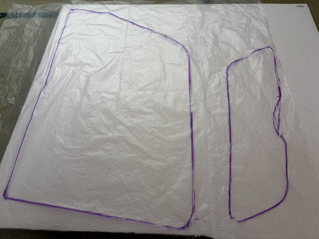 発泡スチロールの上に、車の窓枠の形を紫色のマジックでなぞったゴミ袋を乗せている様子