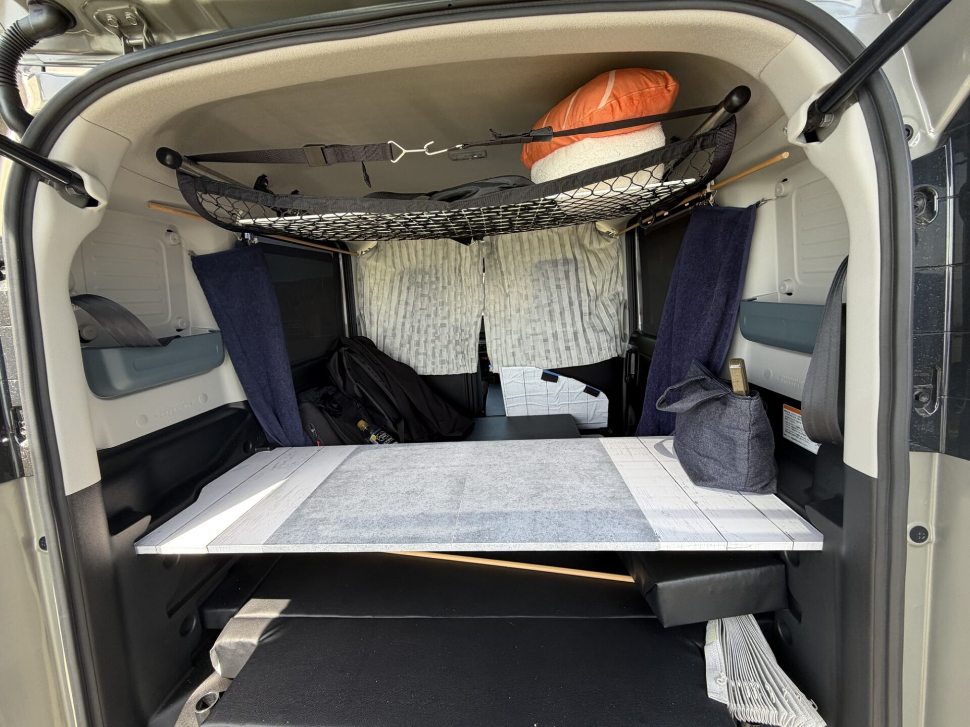 スペーシアベースの車内後方の全景。自作のテーブルと、天井に設置されたルーフネット収納が見える。
