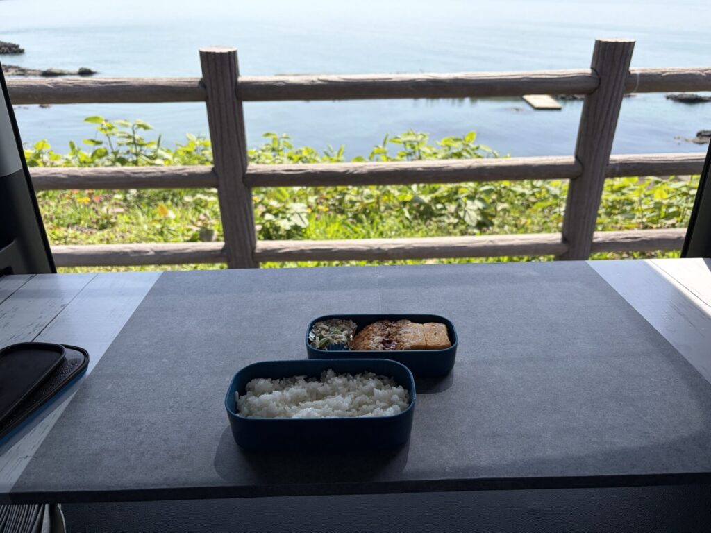 石目調のリメイクシートを貼った自作テーブルの上にお弁当を置き、バックドアから海を眺める様子