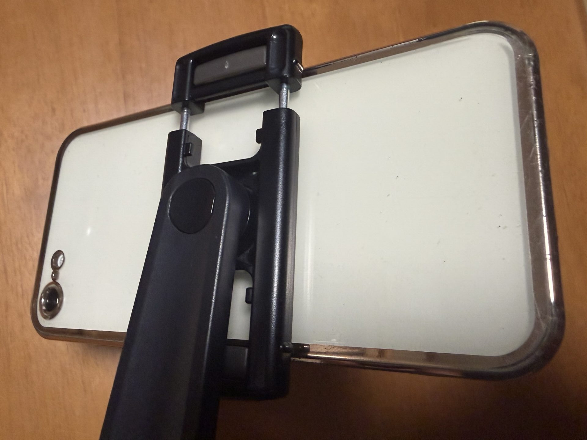 自撮り棒のバネ式ホルダーに、黒いスマホをしっかりと挟んで固定している様子
