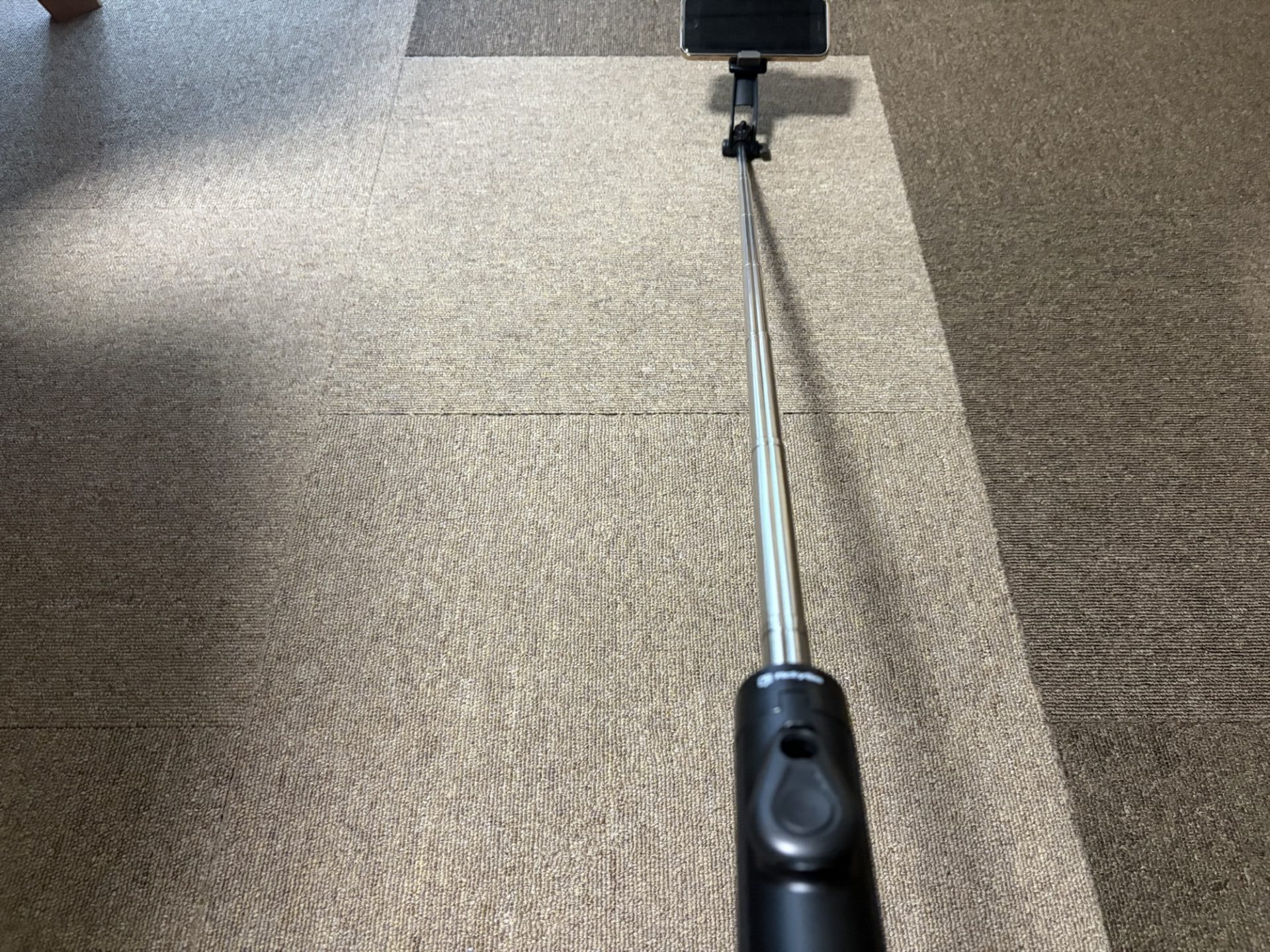 自撮り棒の金属製の棒（ポール）を途中まで伸ばし、スマホを構えている状態