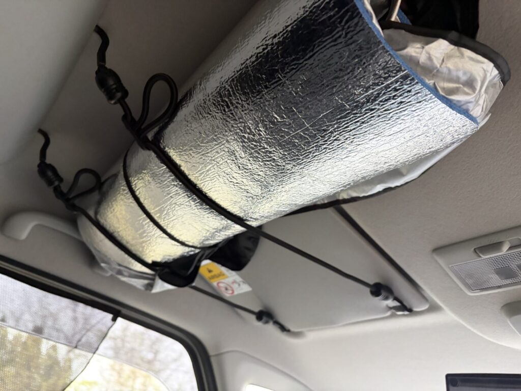 スペーシアベースの助手席側頭上の空間に、ゴムロープを使って丸めた銀マット製サンシェードを固定している様子