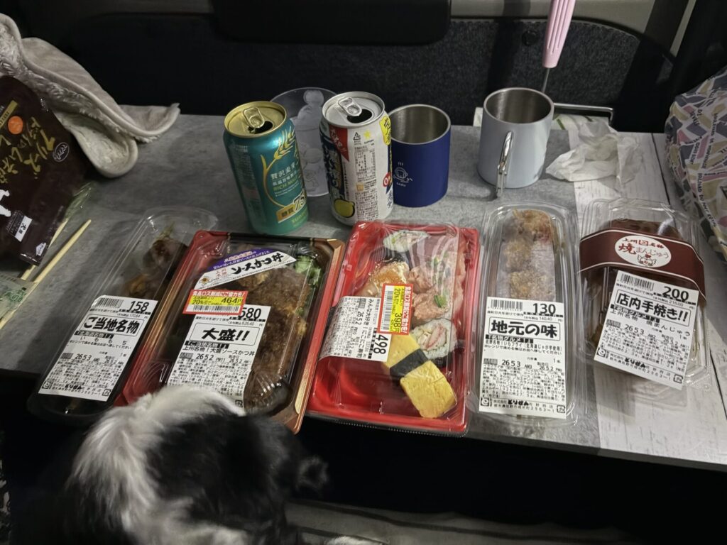 車内のテーブルにズラリと並べられた、ソースかつ丼、お寿司、焼きまんじゅうなどのご当地グルメとノンアルコールビール