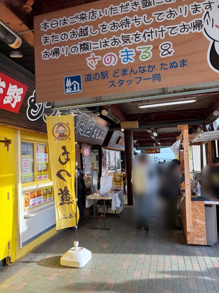  活気ある「道の駅 どまんなか たぬま」の軒先と、「もつ煮」などの美味しそうなのぼり旗