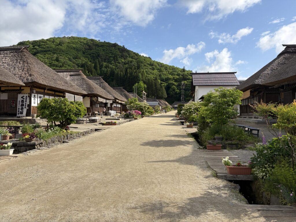 茅葺き屋根の民家が並ぶ大内宿の入り口と、サラサラと水が流れる道路脇の水路