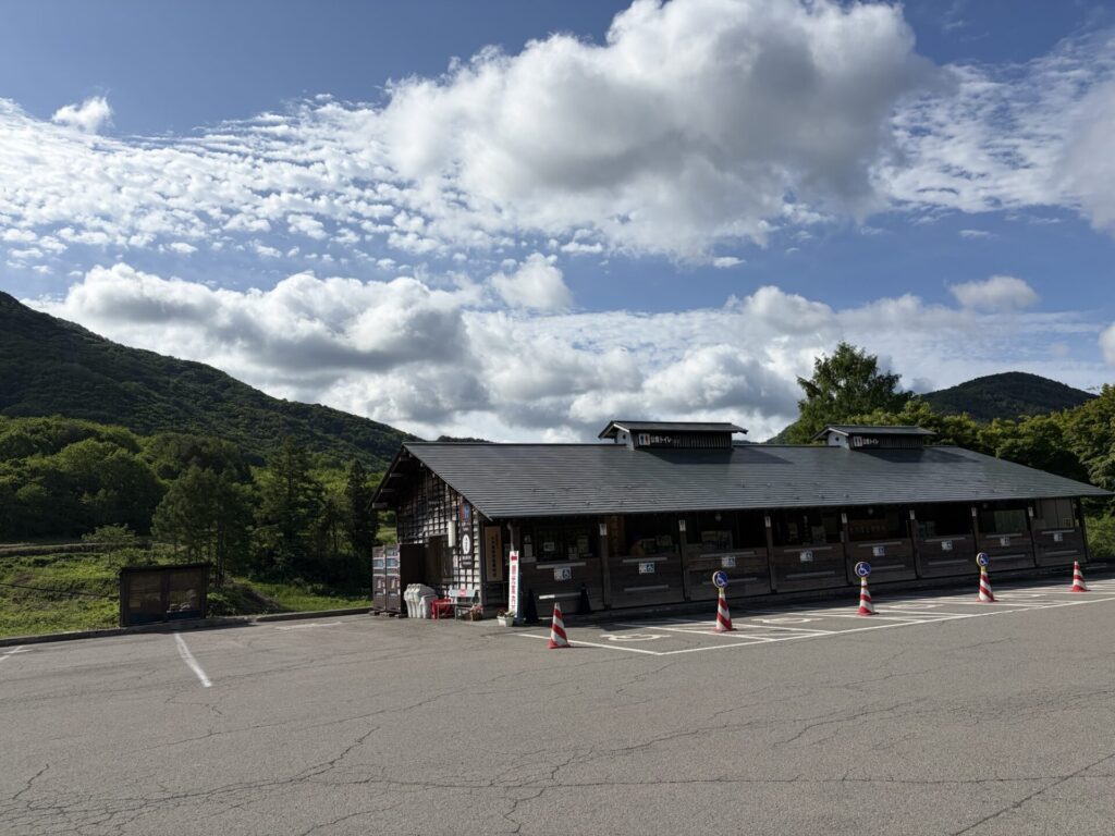 青空の下に広がる福島県大内宿の広大な普通車用駐車場と山々の景色