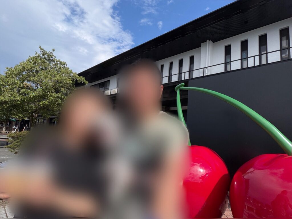 さくらんぼの大きなモニュメントの前で愛犬を抱っこする夫婦